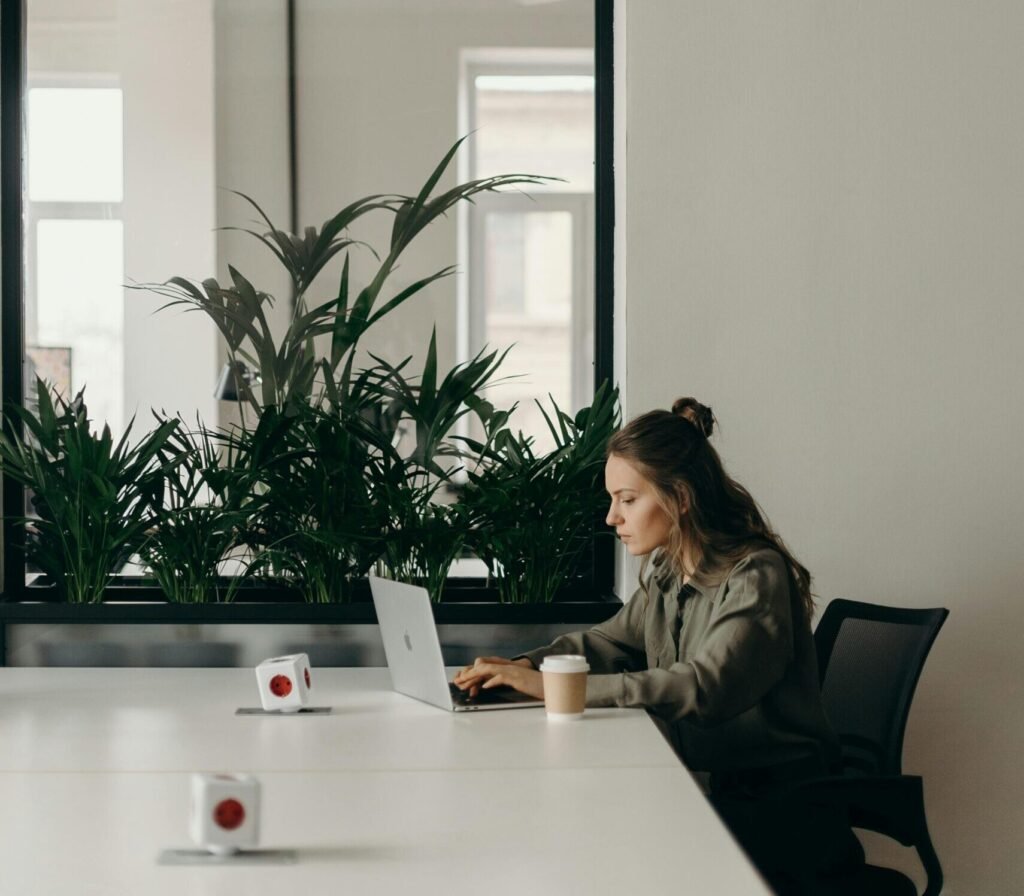 Woman working on a laptop in a minimalist home office with plants.